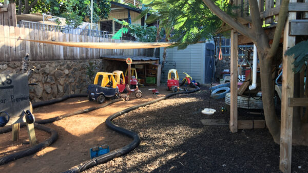 Playground at a family child care home in Hawaii. Several children bikes and cars on the play road that includes a home made gas station.