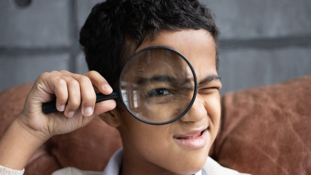 a boy holding magnifying glass up to his eye.